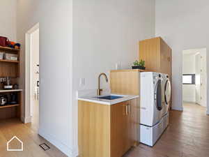 Washroom with cabinets, light wood-type flooring, washer and clothes dryer, and sink