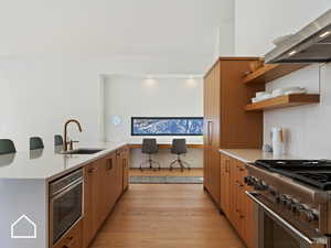 Kitchen with light hardwood / wood-style floors, exhaust hood, sink, stainless steel stove, and oven