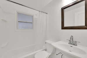 Full bathroom with sink, shower / bathtub combination with curtain, and toilet