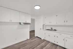 Kitchen featuring light wood-type flooring, white cabinetry, sink, and tasteful backsplash