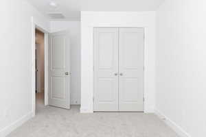 Unfurnished bedroom with light carpet and a closet