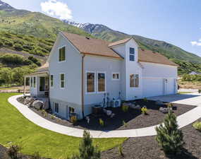 View of side of home with a mountain view, a yard, a garage, and central AC unit