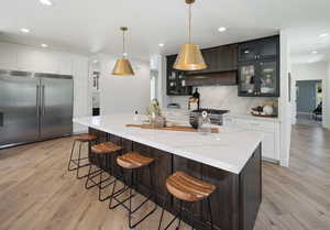 Kitchen with light stone counters, an island with sink, pendant lighting, and premium appliances