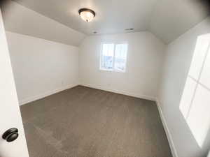 Bonus room with lofted ceiling and dark colored carpet