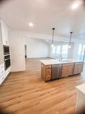 Kitchen with sink, white cabinetry, light hardwood / wood-style flooring, pendant lighting, and appliances with stainless steel finishes