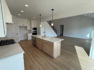 Kitchen with stainless steel appliances, sink, a center island with sink, white cabinets, and light hardwood / wood-style floors