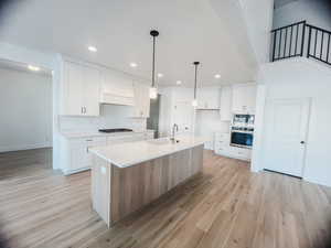 Kitchen featuring sink, white cabinets, an island with sink, custom exhaust hood, and appliances with stainless steel finishes