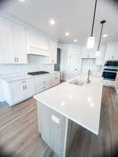 Kitchen featuring stainless steel appliances, premium range hood, a center island with sink, and white cabinetry