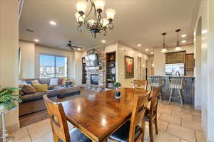 Tiled dining area featuring built in shelves, a stone fireplace, ornamental molding, and ceiling fan with notable chandelier