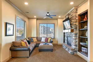 Living room featuring a stone fireplace, ceiling fan, carpet, and ornamental molding