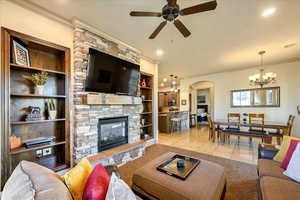 Living room with ceiling fan with notable chandelier, crown molding, built in shelves, light tile patterned floors, and a fireplace