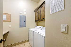 Laundry area with electric panel, light tile patterned flooring, cabinets, and independent washer and dryer