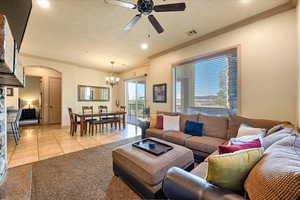 Living room featuring light tile patterned floors, ceiling fan with notable chandelier, a textured ceiling, and ornamental molding