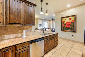 Kitchen featuring stainless steel dishwasher, ceiling fan, light stone counters, and sink