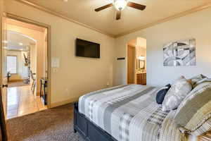 Bedroom with light colored carpet, ensuite bath, ceiling fan, and ornamental molding