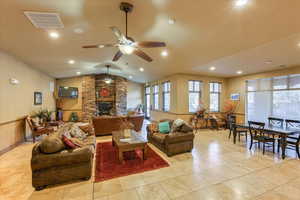 Living room featuring a stone fireplace, ceiling fan, and vaulted ceiling