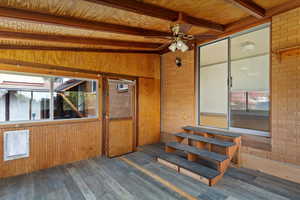 Unfurnished sunroom featuring vaulted ceiling with beams, ceiling fan, and wooden ceiling