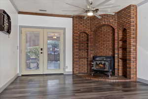 Unfurnished living room featuring a wood stove, dark wood-type flooring, french doors, crown molding, and a textured ceiling