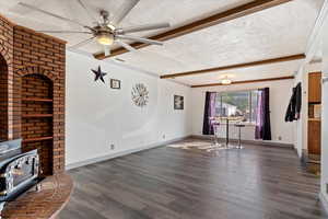 Unfurnished living room featuring dark hardwood / wood-style floors, beam ceiling, a wood stove, and a textured ceiling