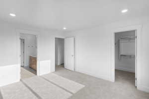 Unfurnished bedroom with light carpet, a walk in closet, ensuite bathroom, and a closet