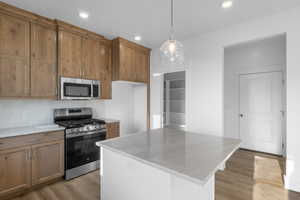 Kitchen with pendant lighting, a center island, light wood-type flooring, and appliances with stainless steel finishes