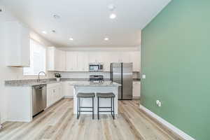 Kitchen with a kitchen bar, appliances with stainless steel finishes, light hardwood / wood-style flooring, a center island, and white cabinetry