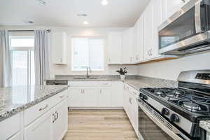 Kitchen with white cabinetry, sink, stainless steel appliances, and light hardwood / wood-style flooring