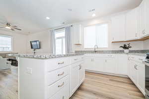 Kitchen featuring ceiling fan, a kitchen island, light stone counters, light hardwood / wood-style flooring, and white cabinets