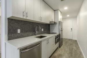 Kitchen with appliances with stainless steel finishes, backsplash, light stone counters, sink, and light hardwood / wood-style flooring