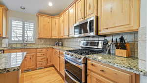 Kitchen with backsplash, light stone countertops, sink, and stainless steel appliances