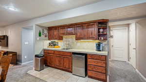 Basement Kitchenette / wet bar area featuring backsplash, light colored carpet, sink, tile countertops, and dishwasher