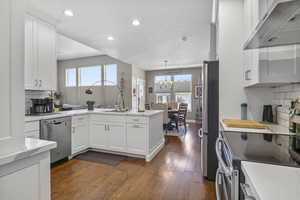 Kitchen with wall chimney exhaust hood, white cabinetry, backsplash, and appliances with stainless steel finishes