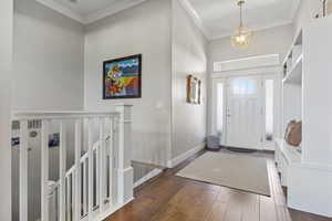 Foyer entrance with ornamental molding, dark wood-type flooring, and an inviting chandelier