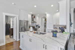 Kitchen with sink, stainless steel appliances, white cabinetry, and wall chimney range hood