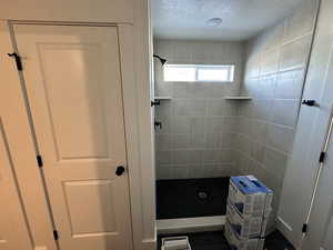 Bathroom featuring tile patterned flooring, a tile shower, and a textured ceiling