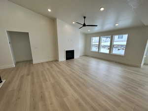 Unfurnished living room featuring a textured ceiling, vaulted ceiling, ceiling fan, and light hardwood / wood-style flooring