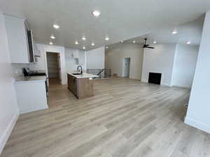 Kitchen with light wood-type flooring, a kitchen island with sink, stainless steel appliances, a textured ceiling, and white cabinets