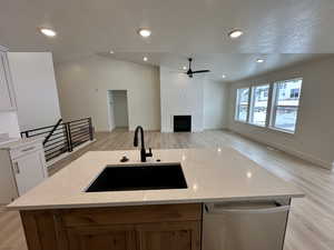 Kitchen featuring vaulted ceiling, sink, stainless steel dishwasher, white cabinets, and light stone countertops