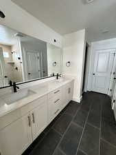 Bathroom featuring tile patterned floors, tiled shower, vanity, and a textured ceiling