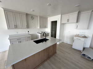 Kitchen featuring a kitchen island with sink, sink, light stone counters, and light hardwood / wood-style floors