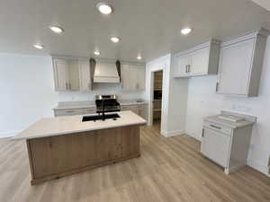 Kitchen with a center island with sink, sink, custom exhaust hood, light wood-type flooring, and stainless steel range oven