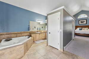 Bathroom featuring tile patterned floors, vanity, a relaxing tiled tub, and lofted ceiling