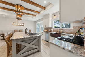 Kitchen with sink, white cabinetry, hanging light fixtures, and light stone counters