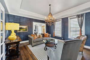 Living room featuring a chandelier, dark hardwood / wood-style flooring, a raised ceiling, and crown molding
