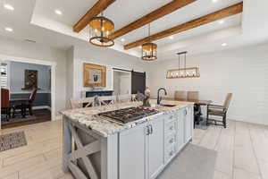 Kitchen featuring a center island with sink, decorative light fixtures, a barn door, and light stone counters