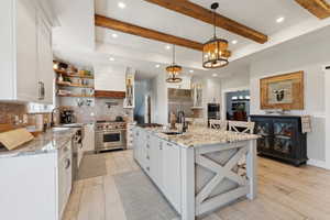 Kitchen featuring white cabinets, premium appliances, hanging light fixtures, and an island with sink