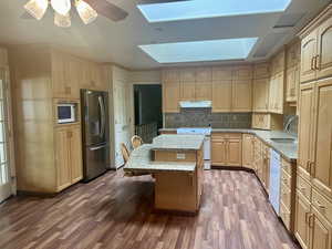 Kitchen featuring a center island, white appliances, dark wood-type flooring, sink, and a skylight