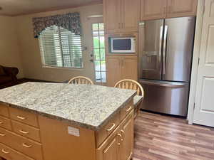 Kitchen featuring a center island, crown molding, stainless steel refrigerator with ice dispenser, light stone countertops, and light hardwood / wood-style floors