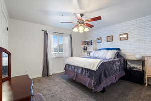 Bedroom with dark colored carpet, ceiling fan, and brick wall