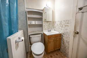 Bathroom featuring vanity, toilet, and tile walls